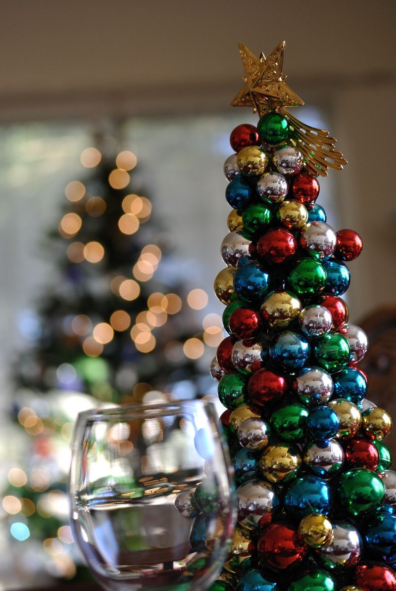 A christmas tree made of beads is on a table next to a glass of wine.