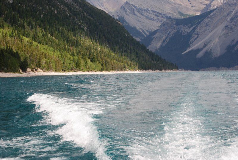 A boat is going through a lake with mountains in the background.