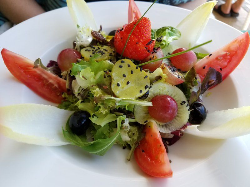 A salad with tomatoes , grapes , kiwi and strawberries on a white plate