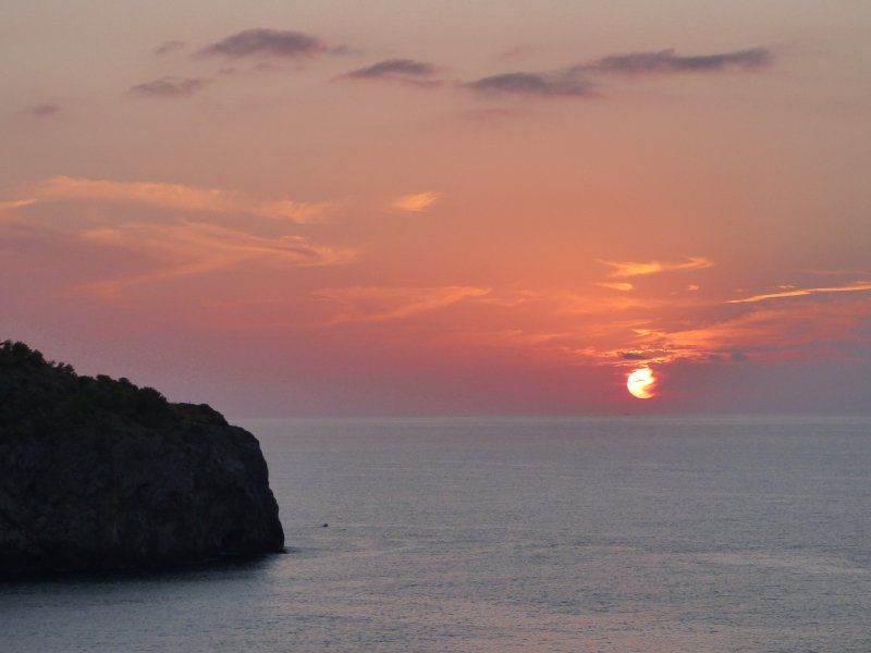 A sunset over the ocean with a cliff in the foreground