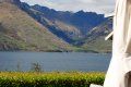 A person is standing in front of a lake with mountains in the background.