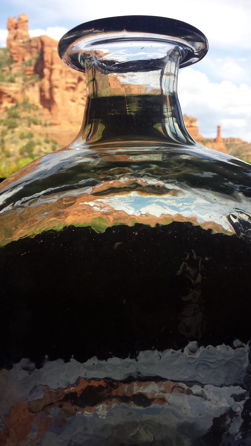 A close up of a glass bottle with a mountain in the background