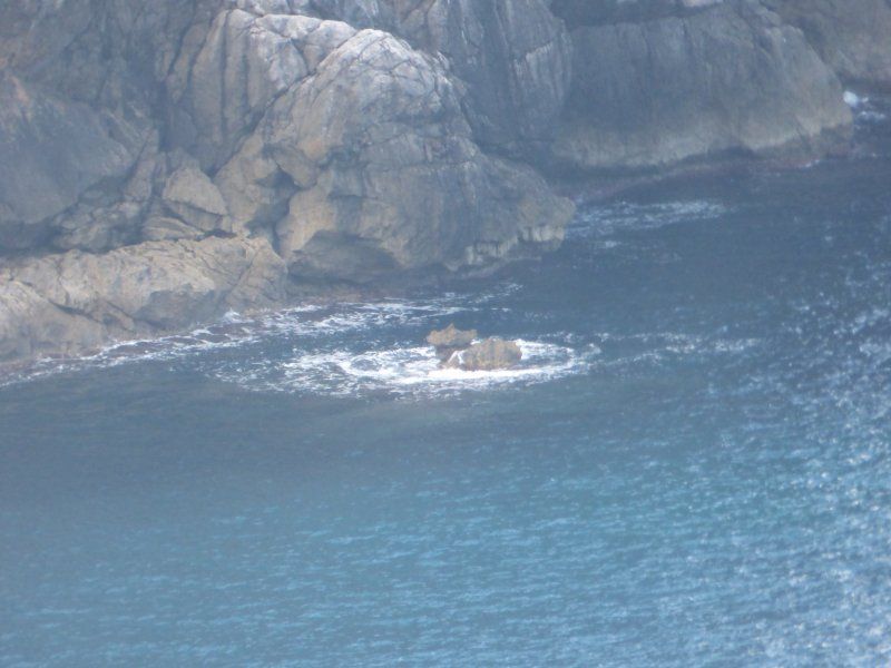 A boat is floating on top of a body of water near a rocky shoreline.
