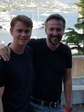 Two men are posing for a picture together in front of a body of water.