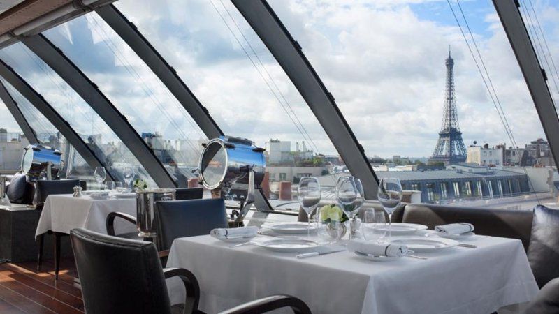 A restaurant with tables and chairs and a view of the eiffel tower.