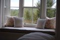 A window seat with pillows and a bed in front of a window.