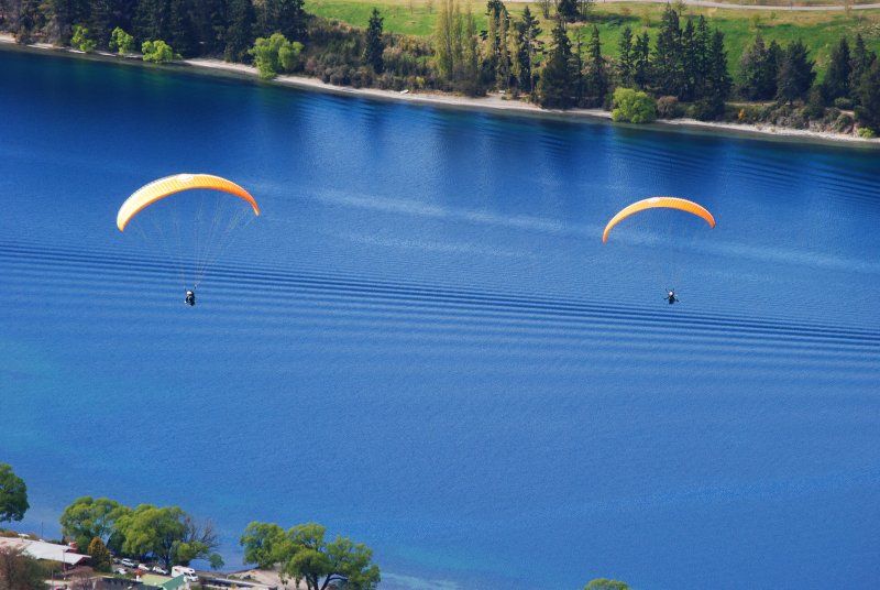 Two paragliders are flying over a large body of water.