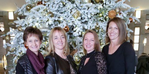 Four women are posing for a picture in front of a christmas tree.