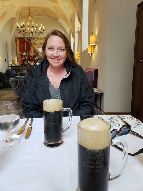 A woman is sitting at a table with two mugs of beer