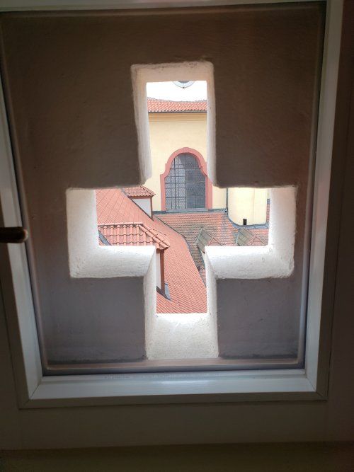 A window with a cross cut out of it and a view of a building.