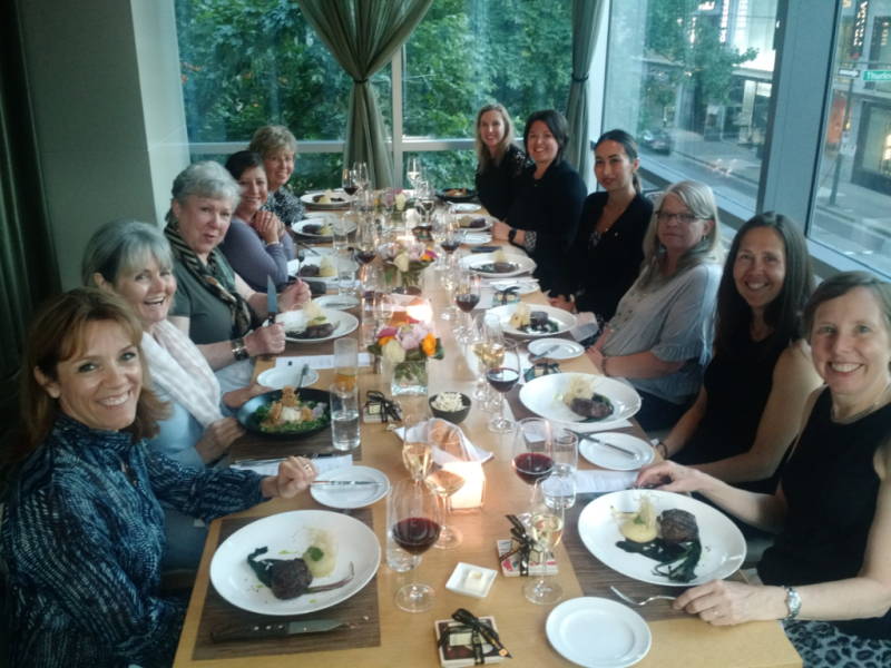 A group of women are sitting at a long table with plates of food and wine glasses