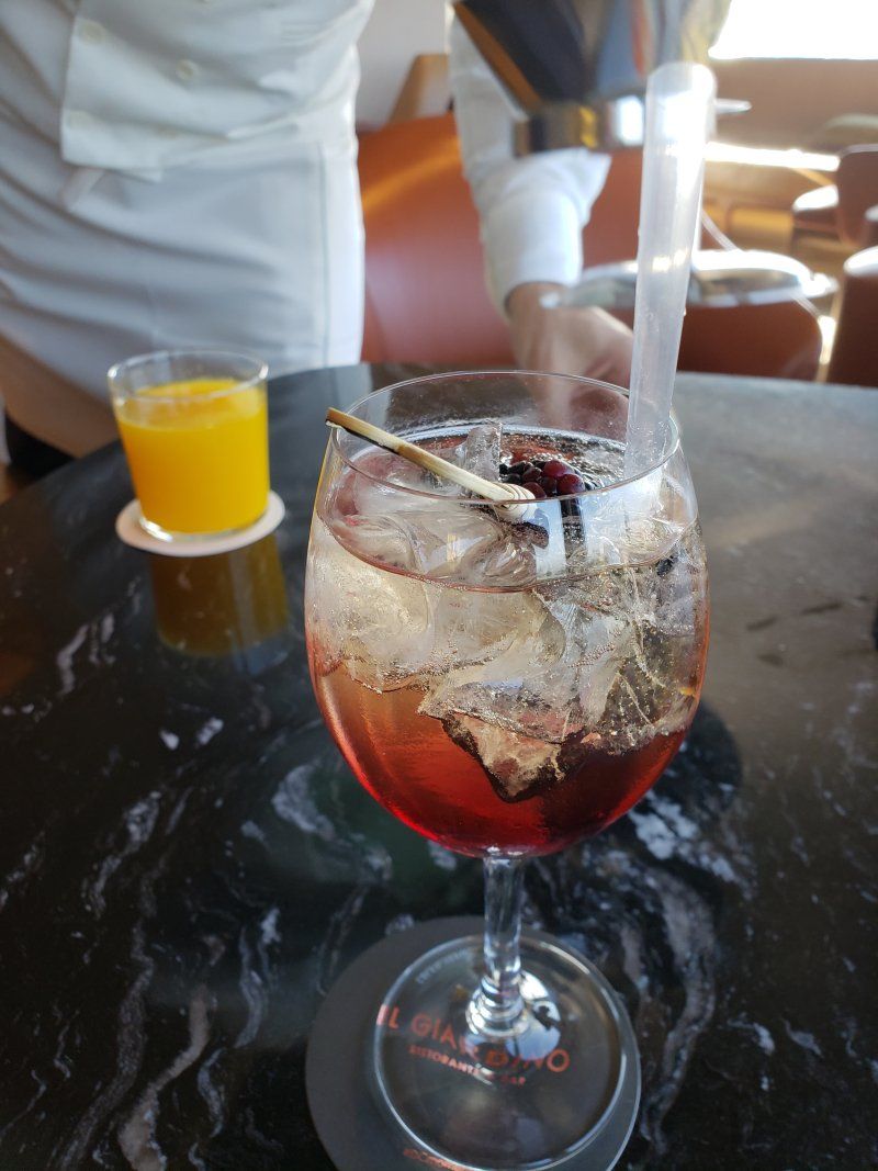 A glass of wine with a straw on a table next to a glass of orange juice