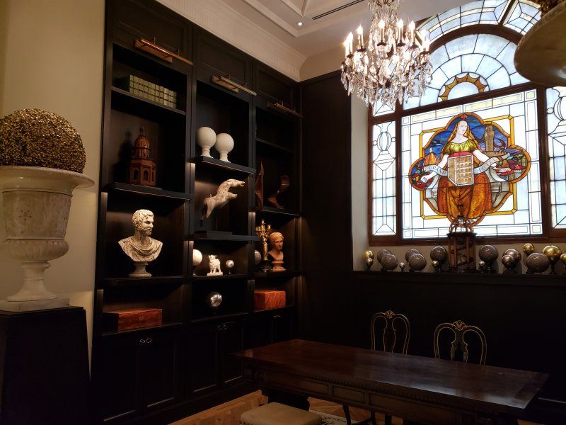 A room with a table , chairs , shelves and a stained glass window.