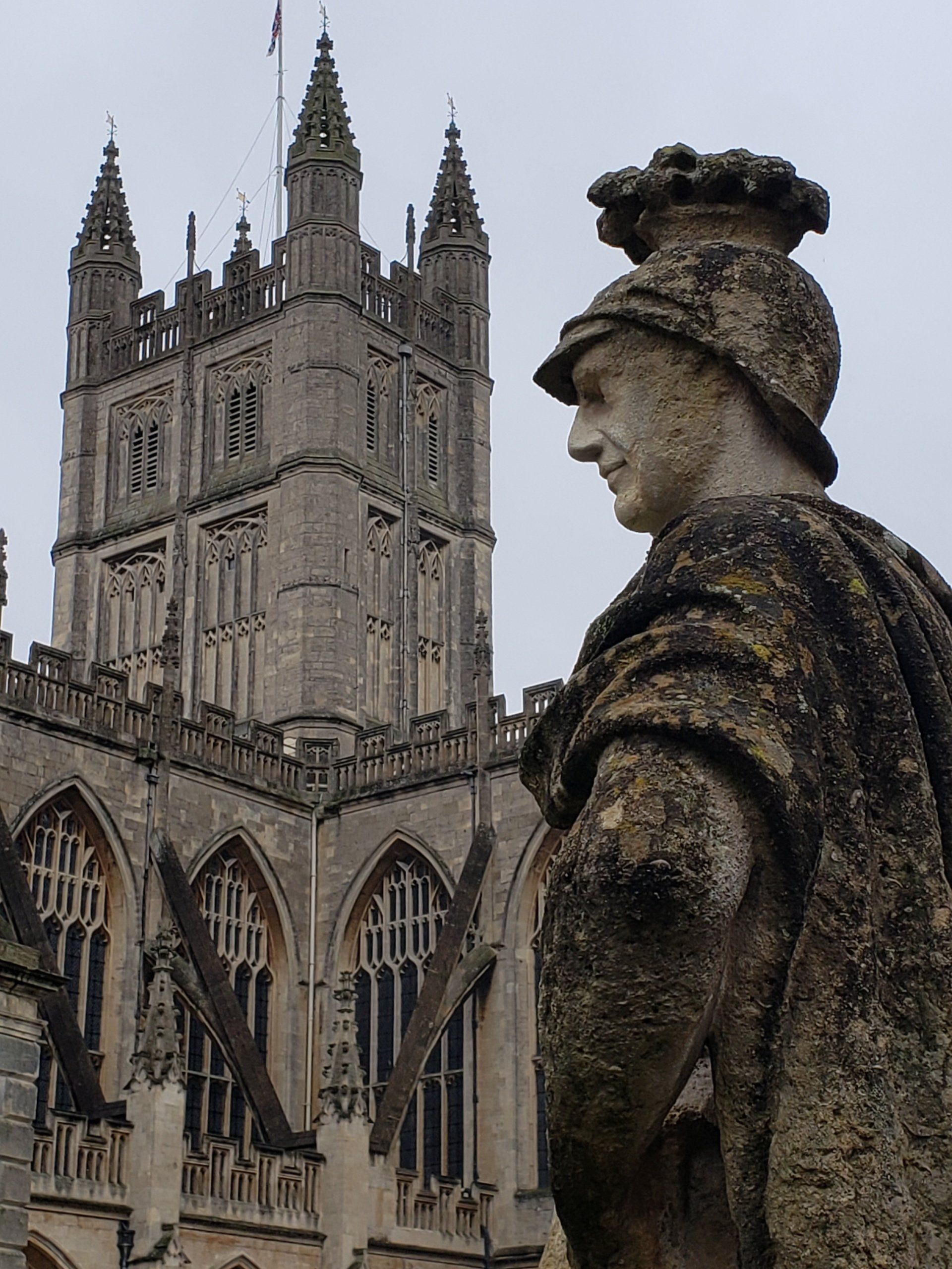 A statue of a man wearing a helmet stands in front of a large building