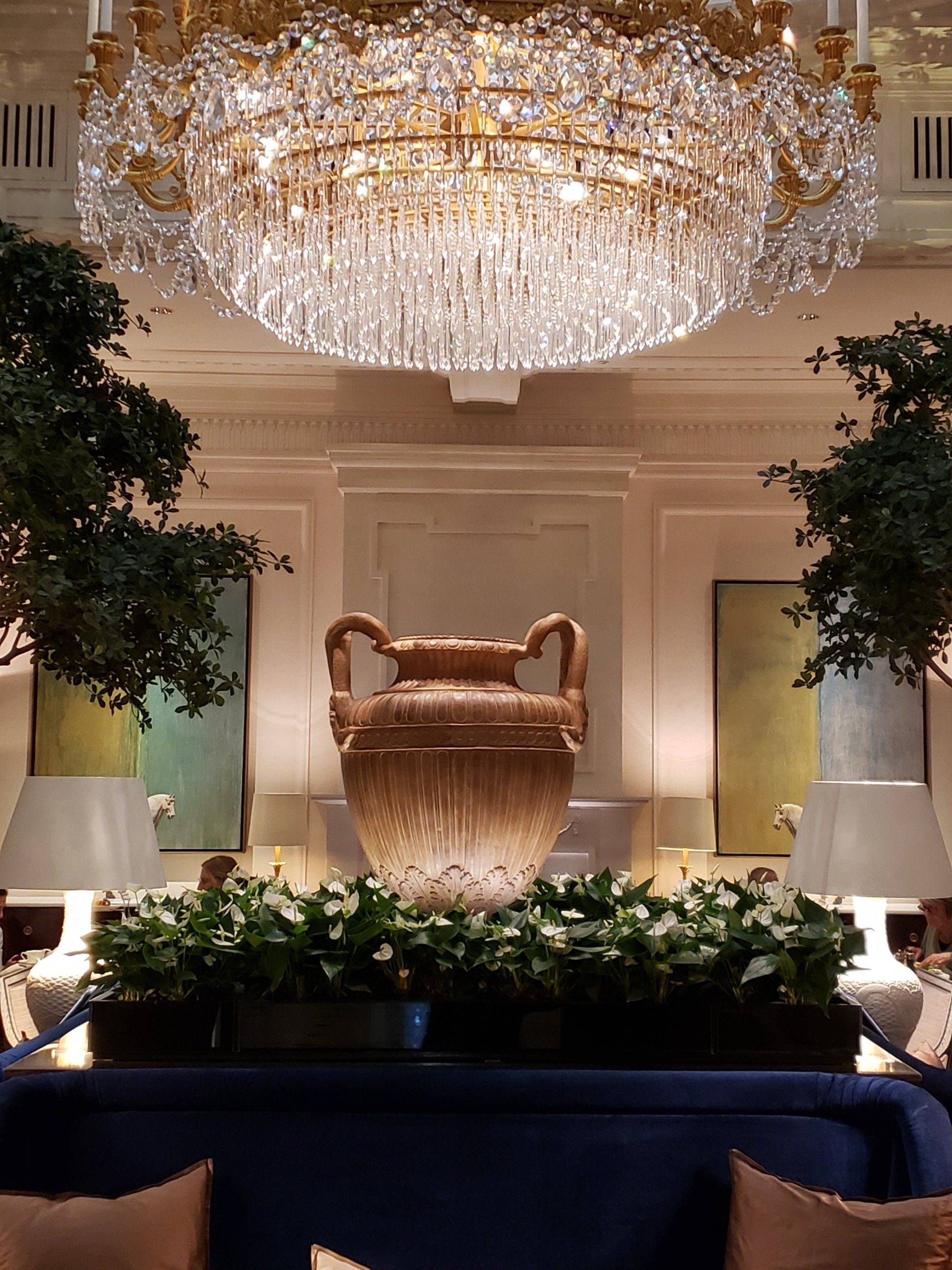 A living room with a chandelier hanging from the ceiling and a vase in the middle.