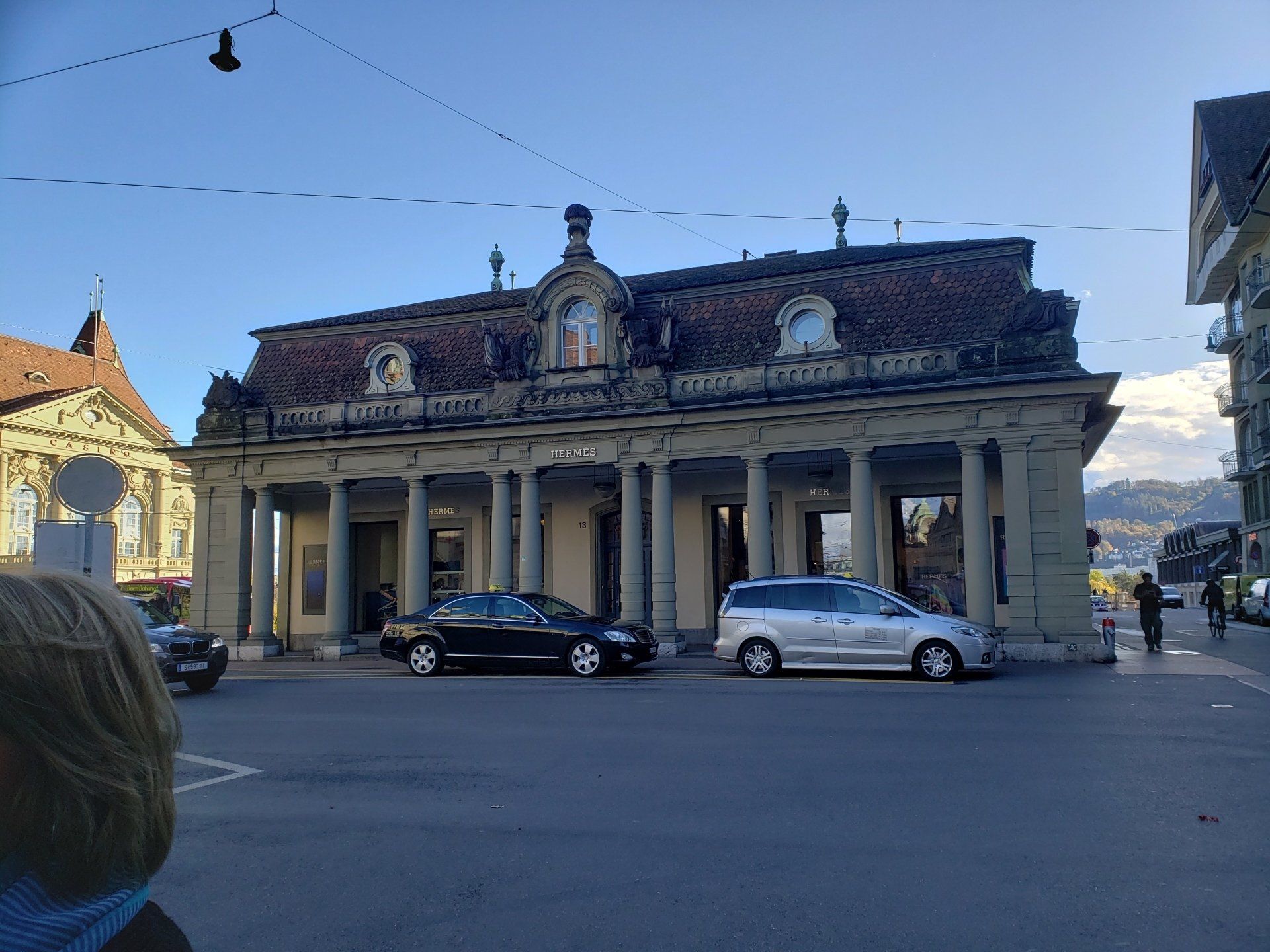 A woman is standing in front of a building with cars parked in front of it.