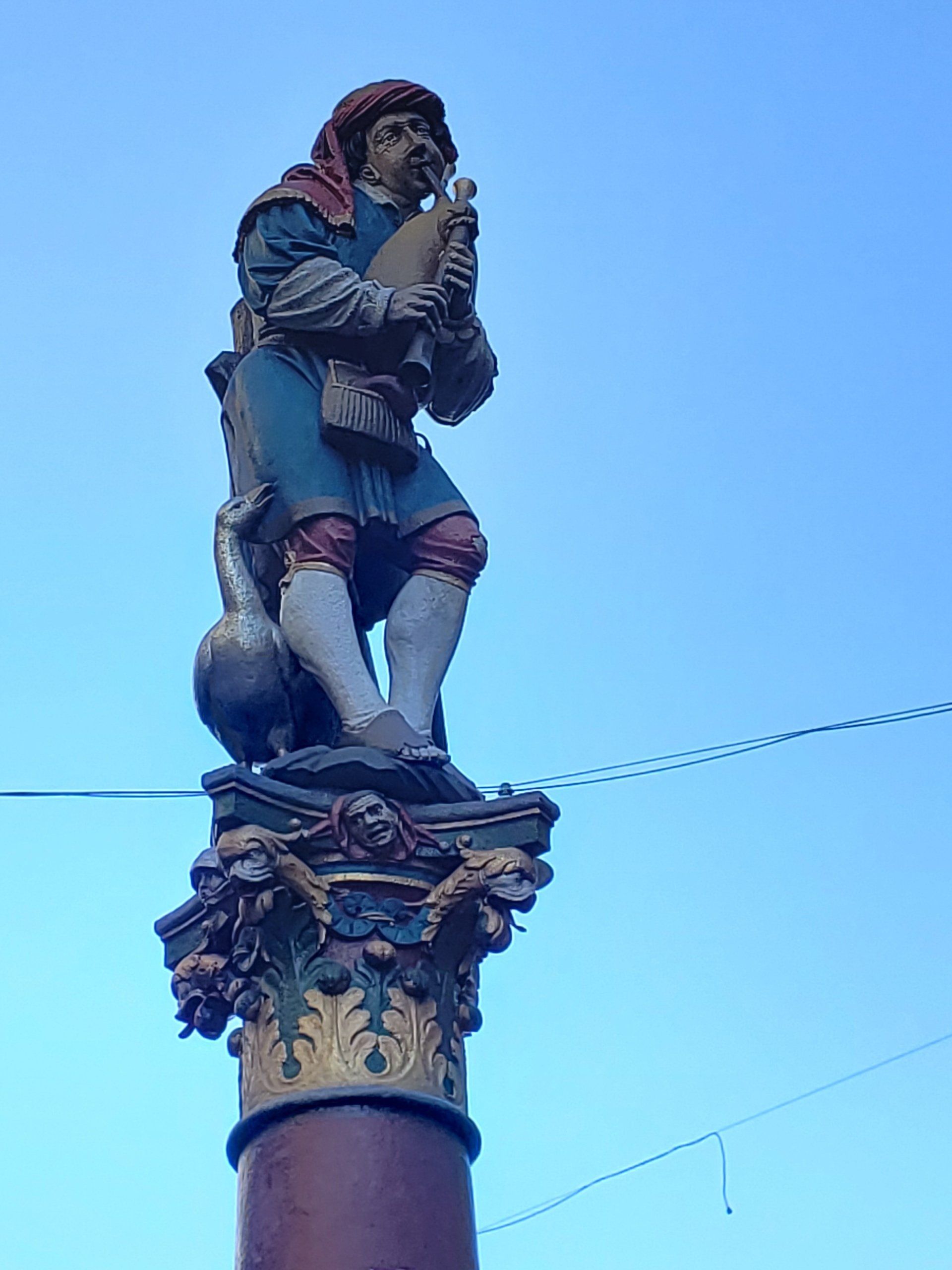 A statue of a man playing a bagpipe on top of a pole.