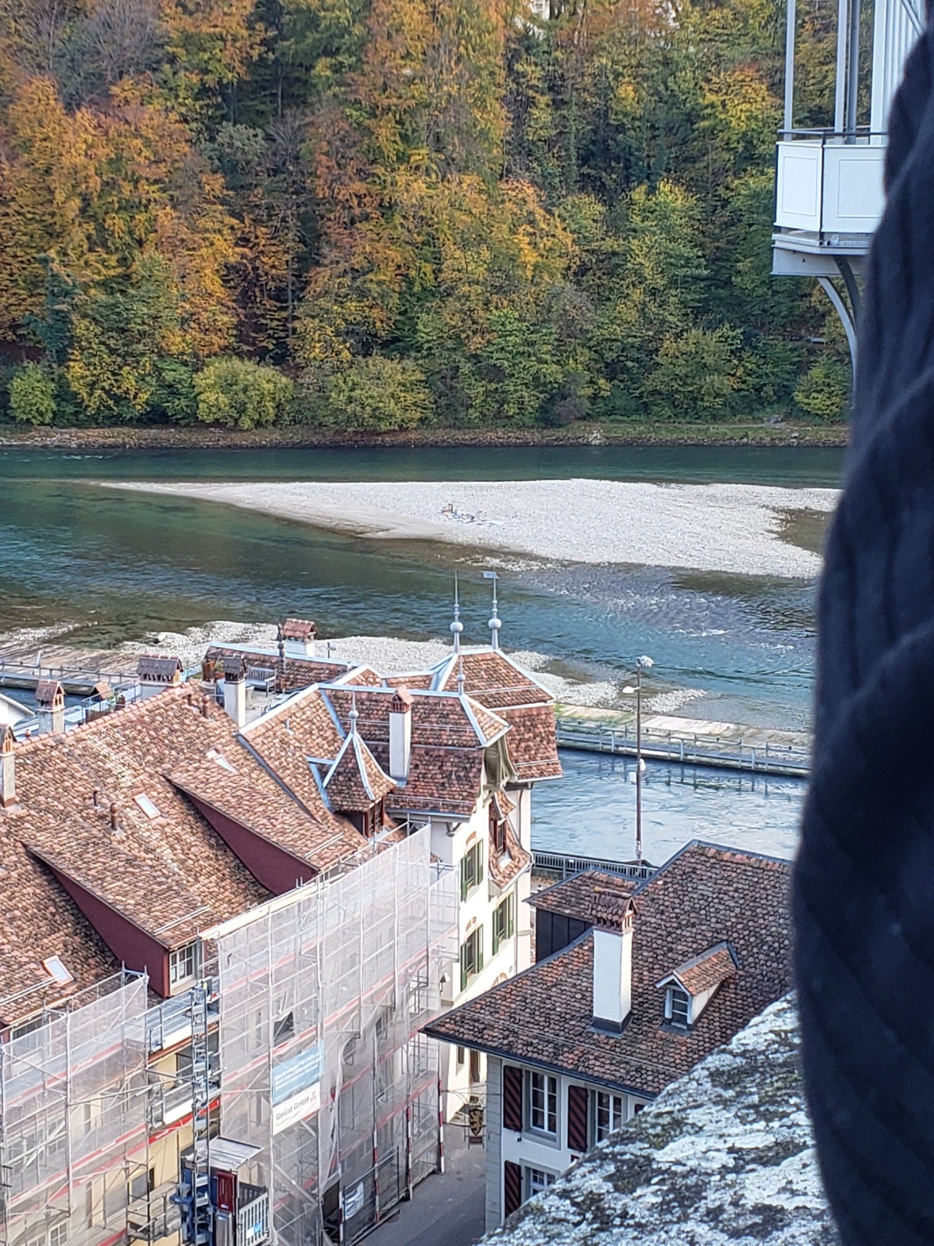 A person is standing on a balcony overlooking a river and a city.