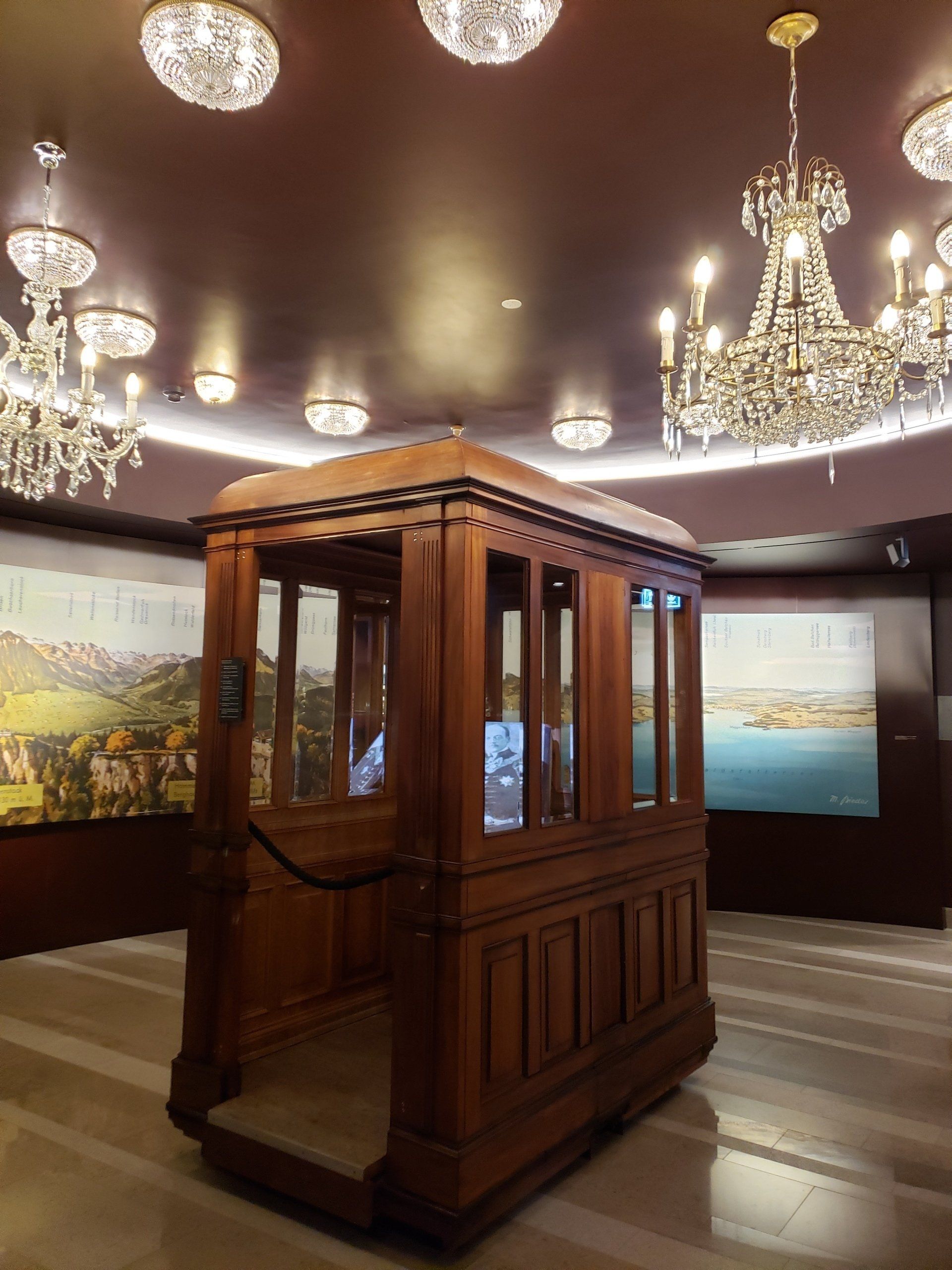 A wooden elevator in a room with chandeliers