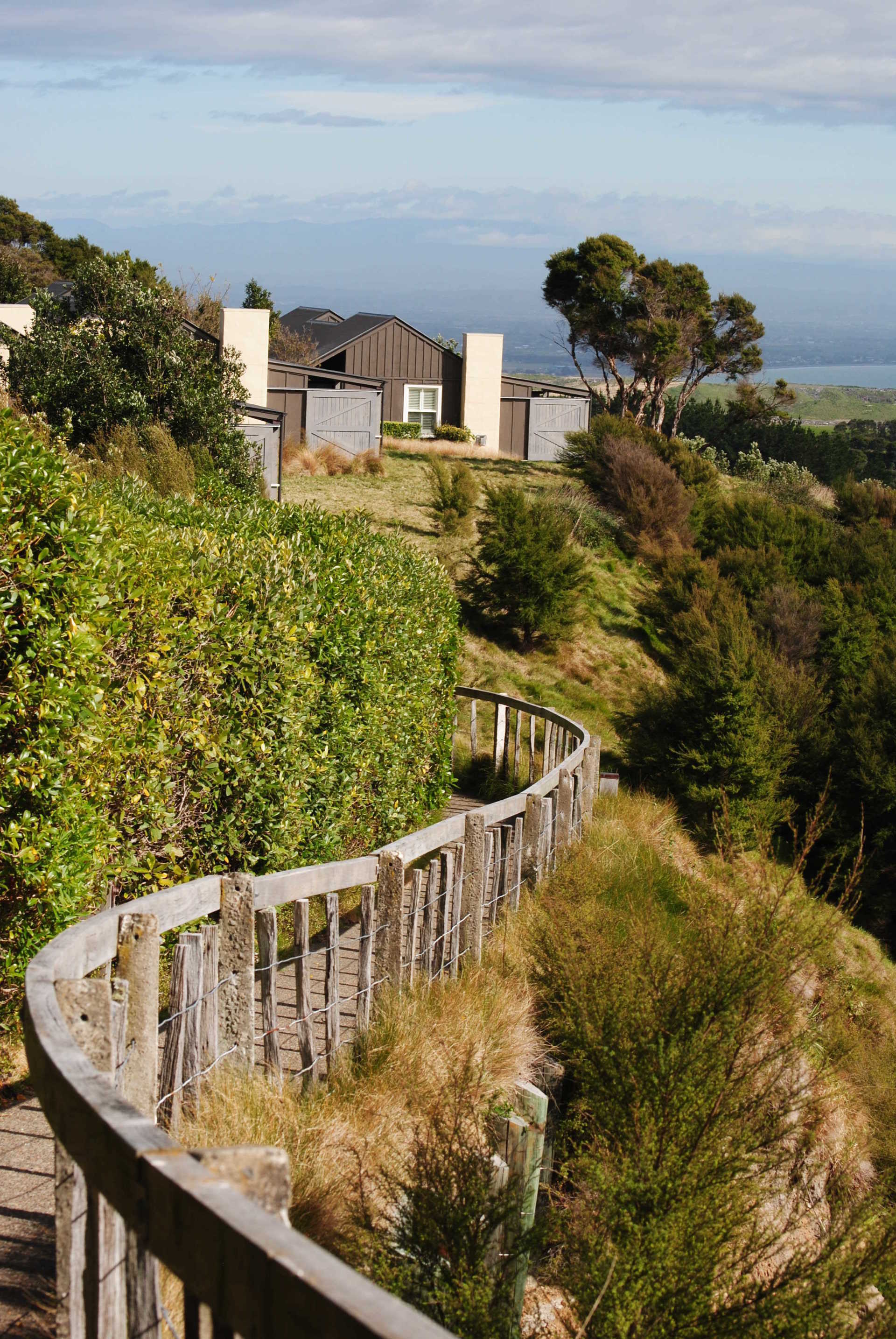 A wooden walkway going up a hill with a house in the background