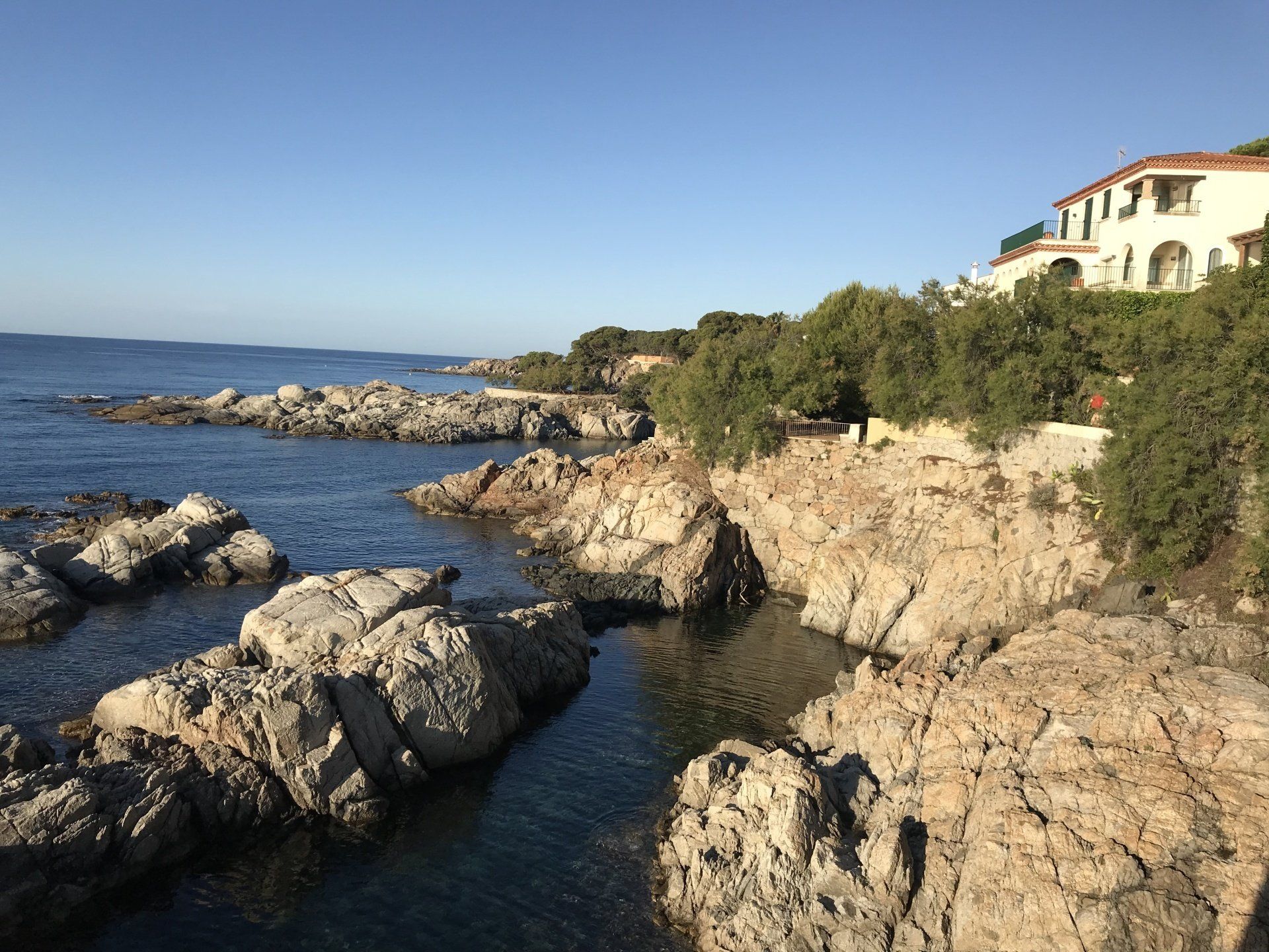 A cliff overlooking a body of water with a house in the background.