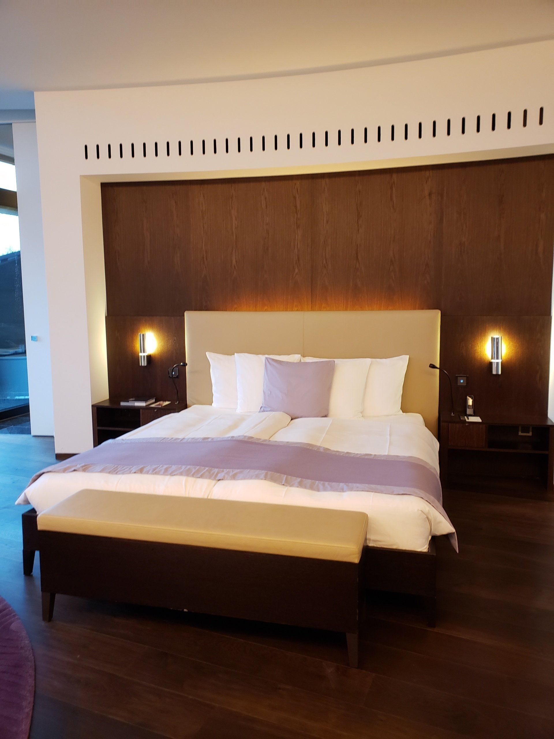 A hotel room with a large bed and a bench