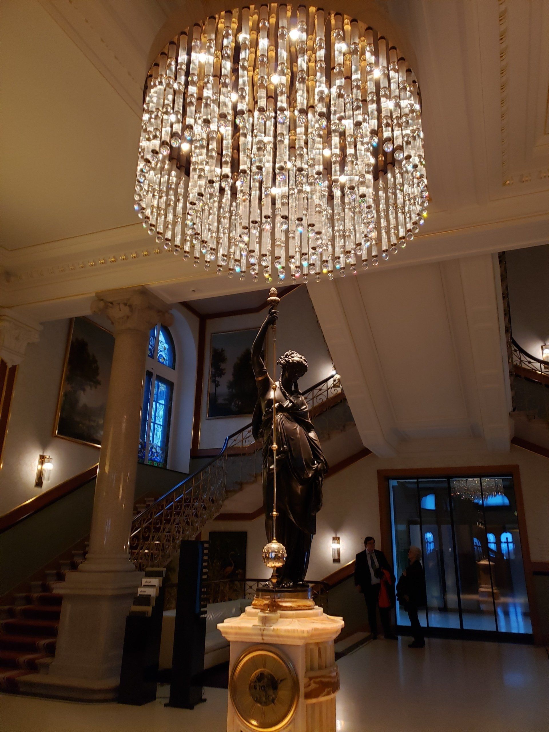 A large chandelier is hanging from the ceiling above a statue in a lobby.