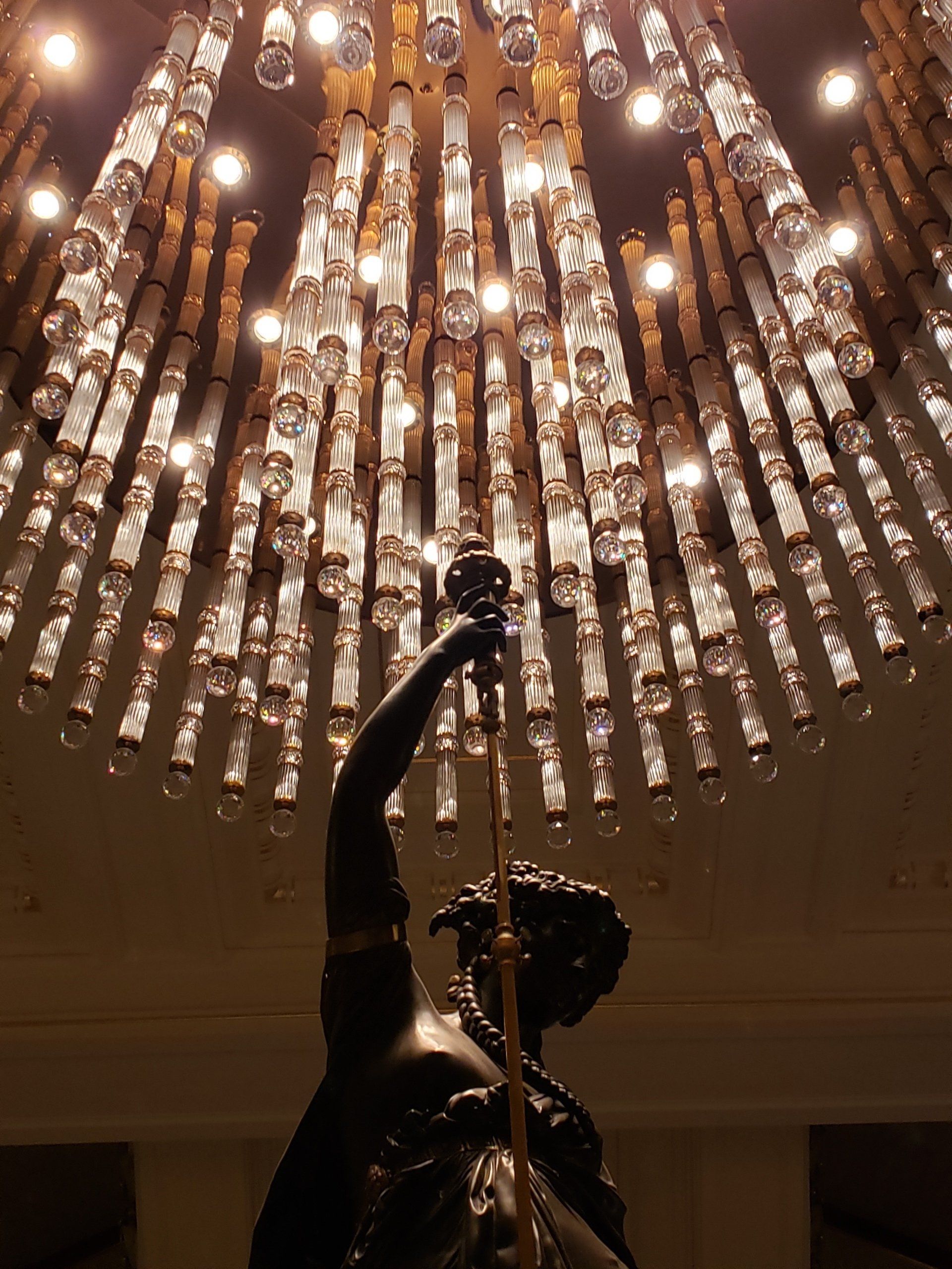 A statue of a woman holding a stick under a chandelier
