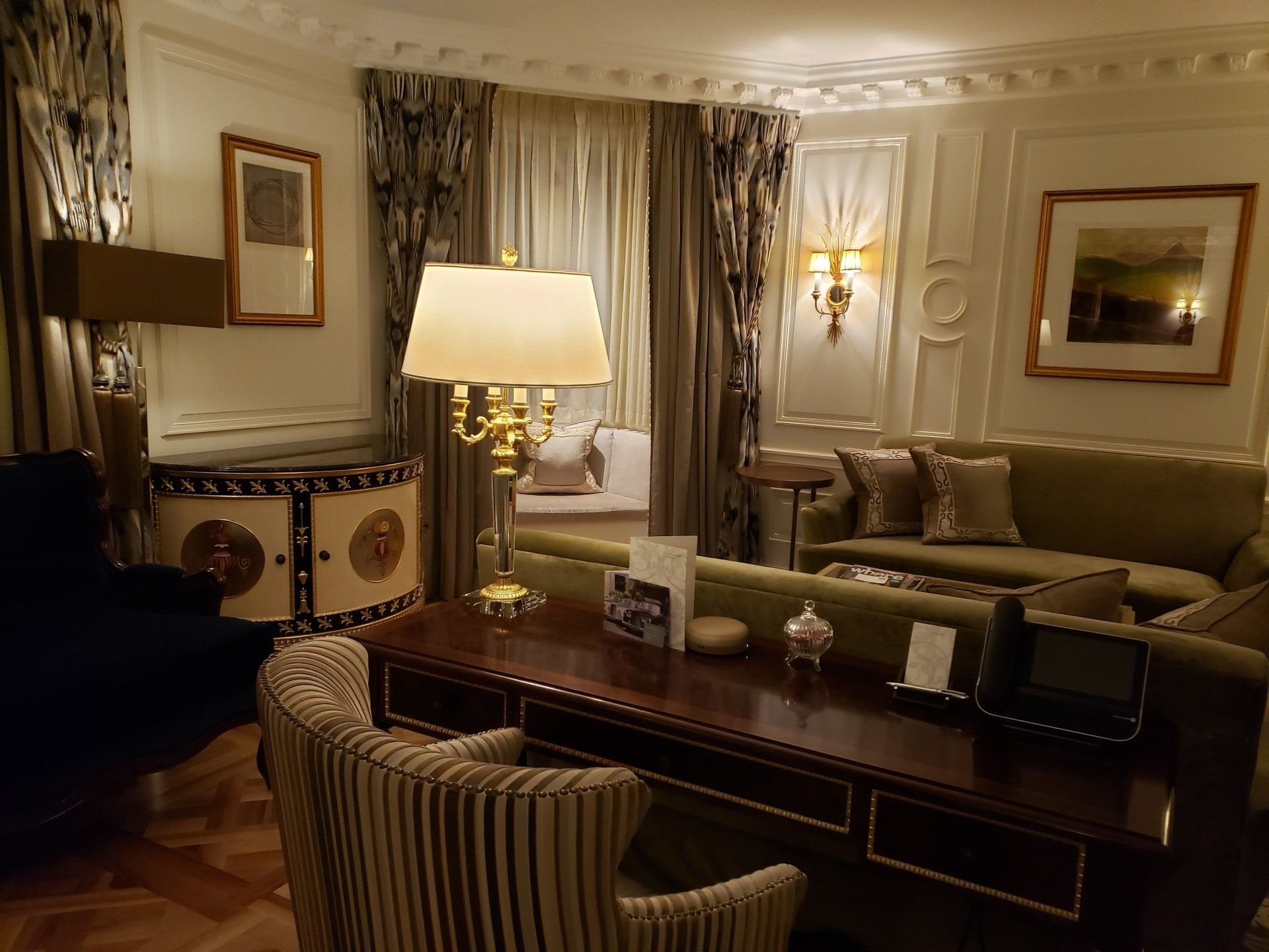 A living room with a desk , chairs , a couch and a lamp.