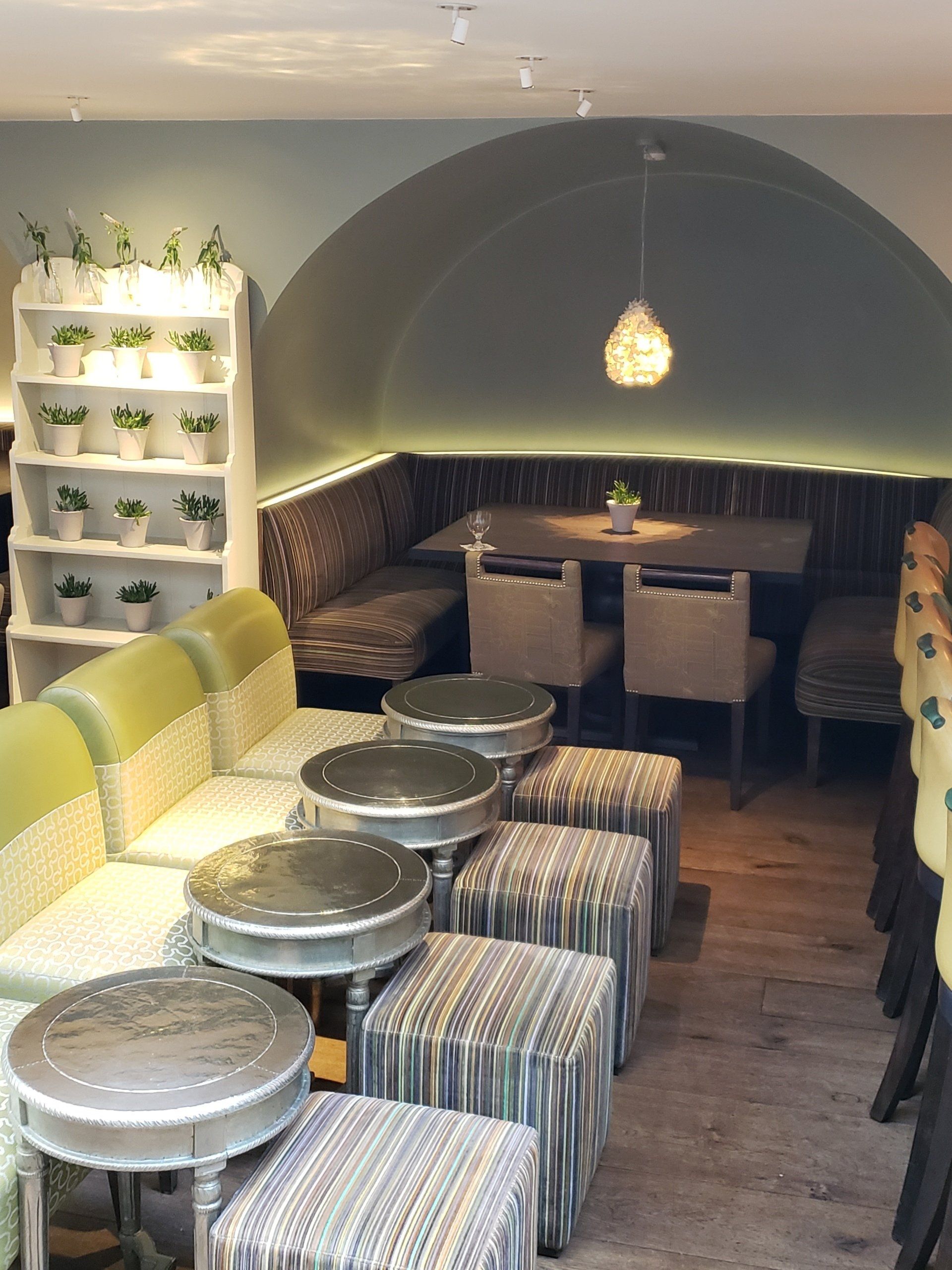 A restaurant with tables and chairs and a shelf full of potted plants