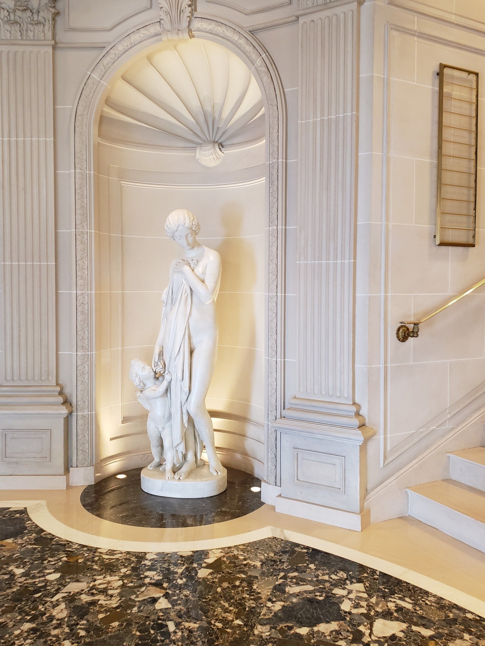 A statue of a woman holding a child in a hallway next to a staircase.