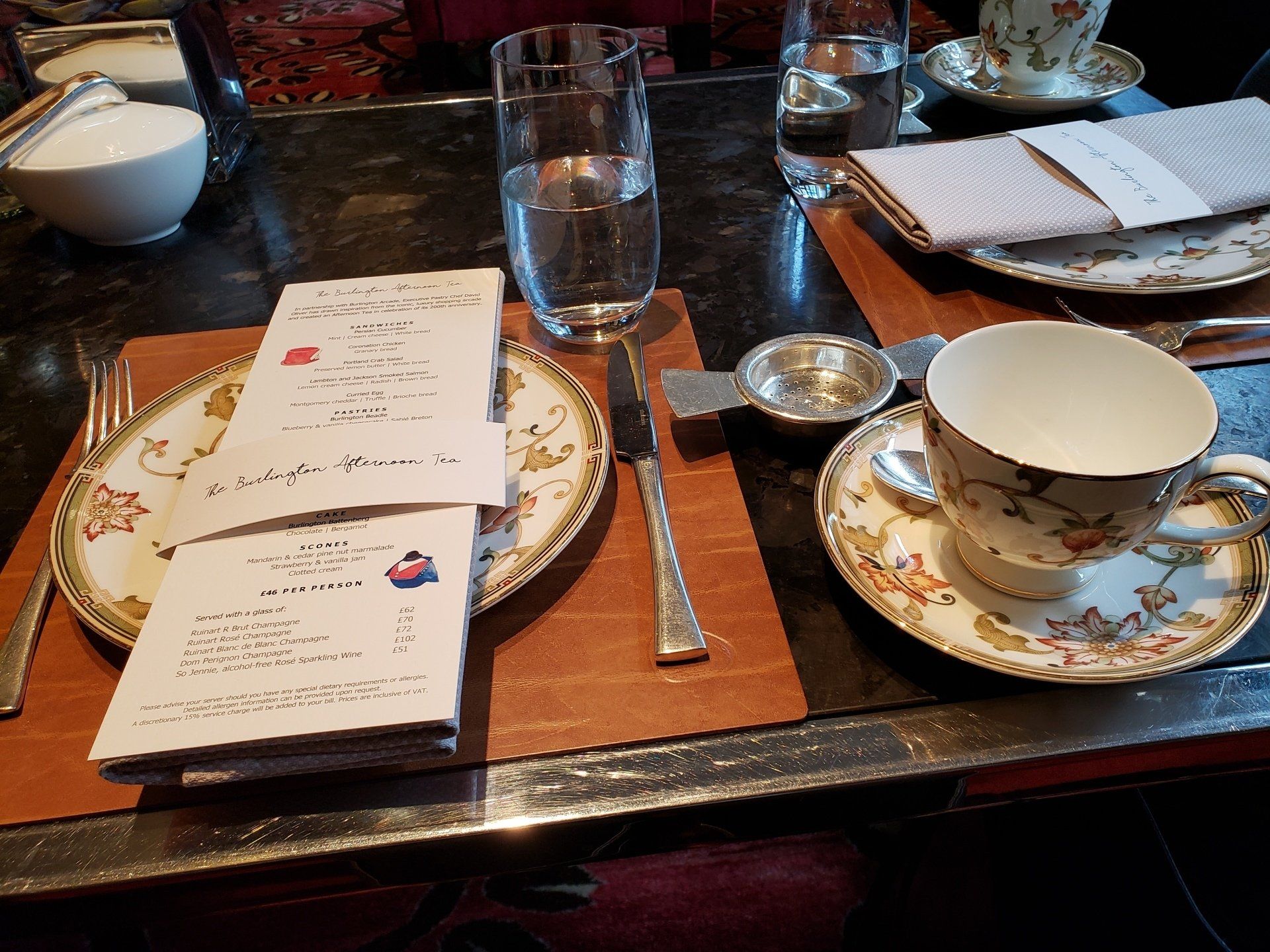 A place setting with plates a cup and saucer a menu and a glass of water