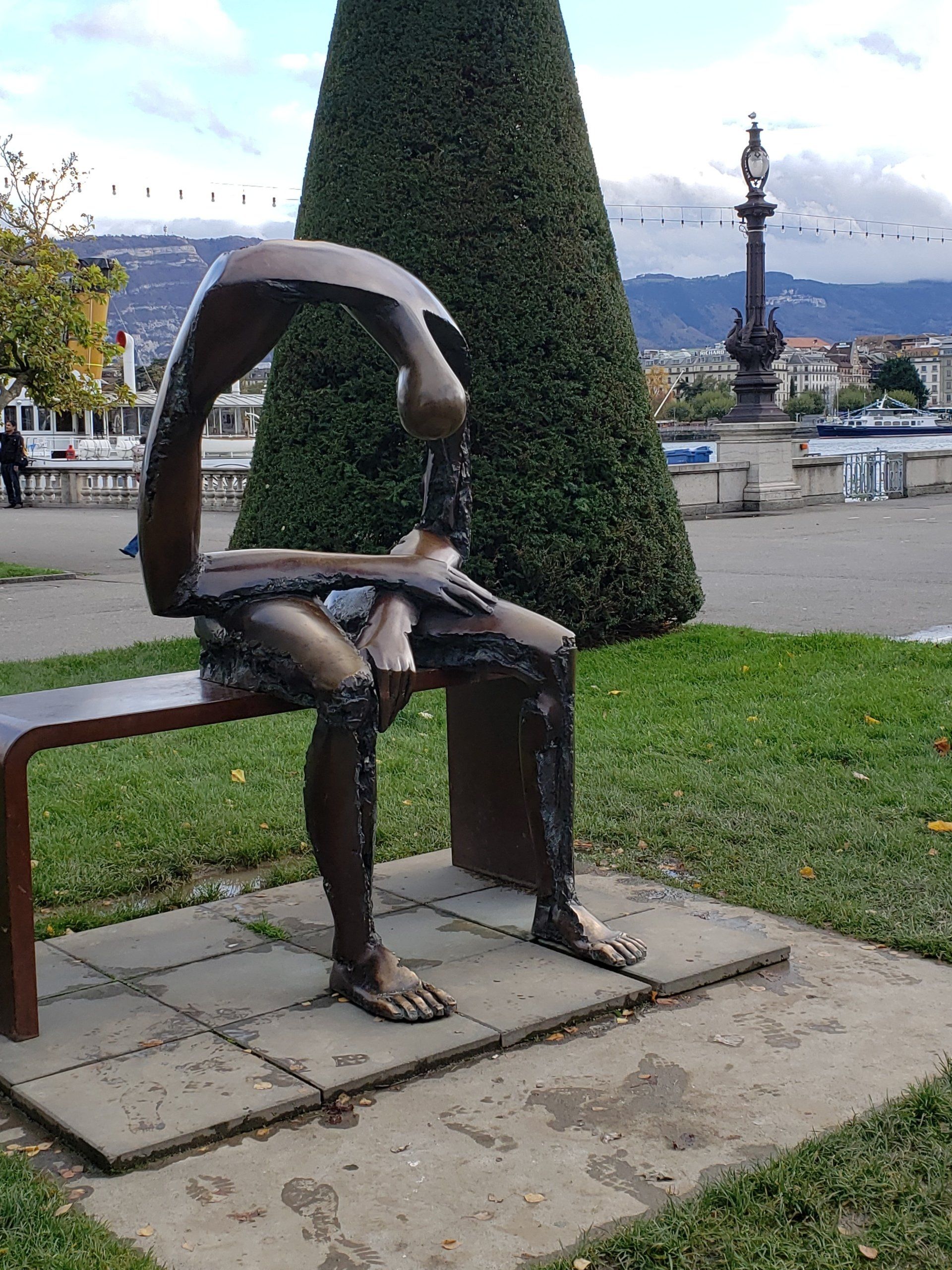 A statue of a person sitting on a bench in a park.