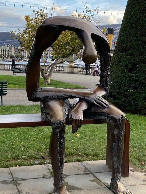 A statue of a person sitting on a bench in a park