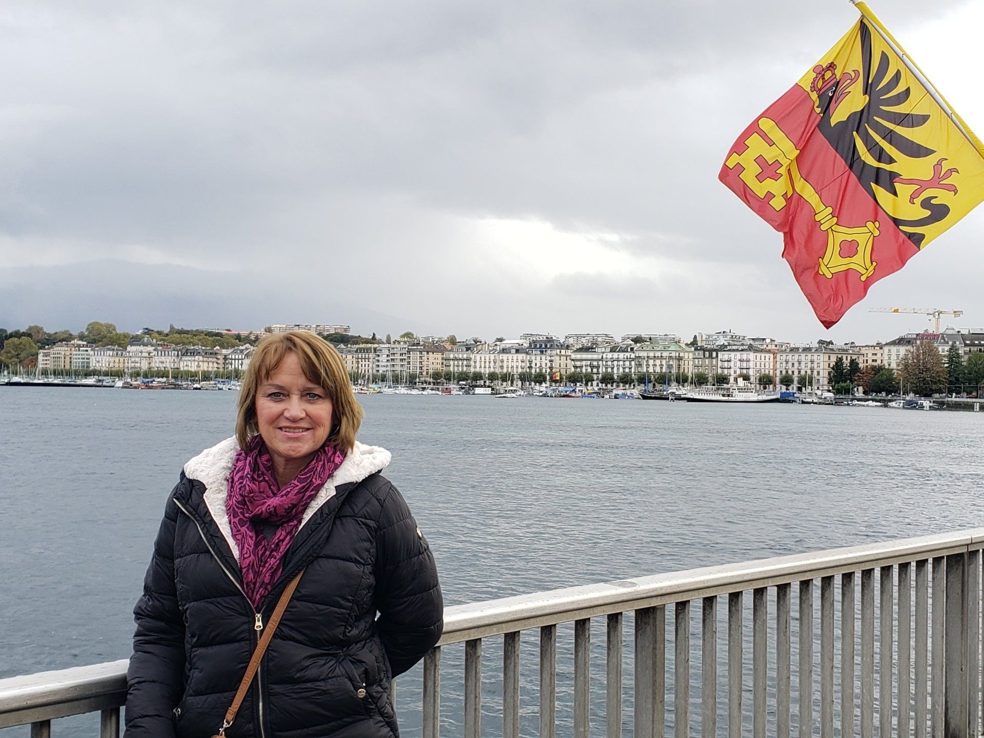 A woman is standing on a bridge overlooking a body of water with a flag in the background.
