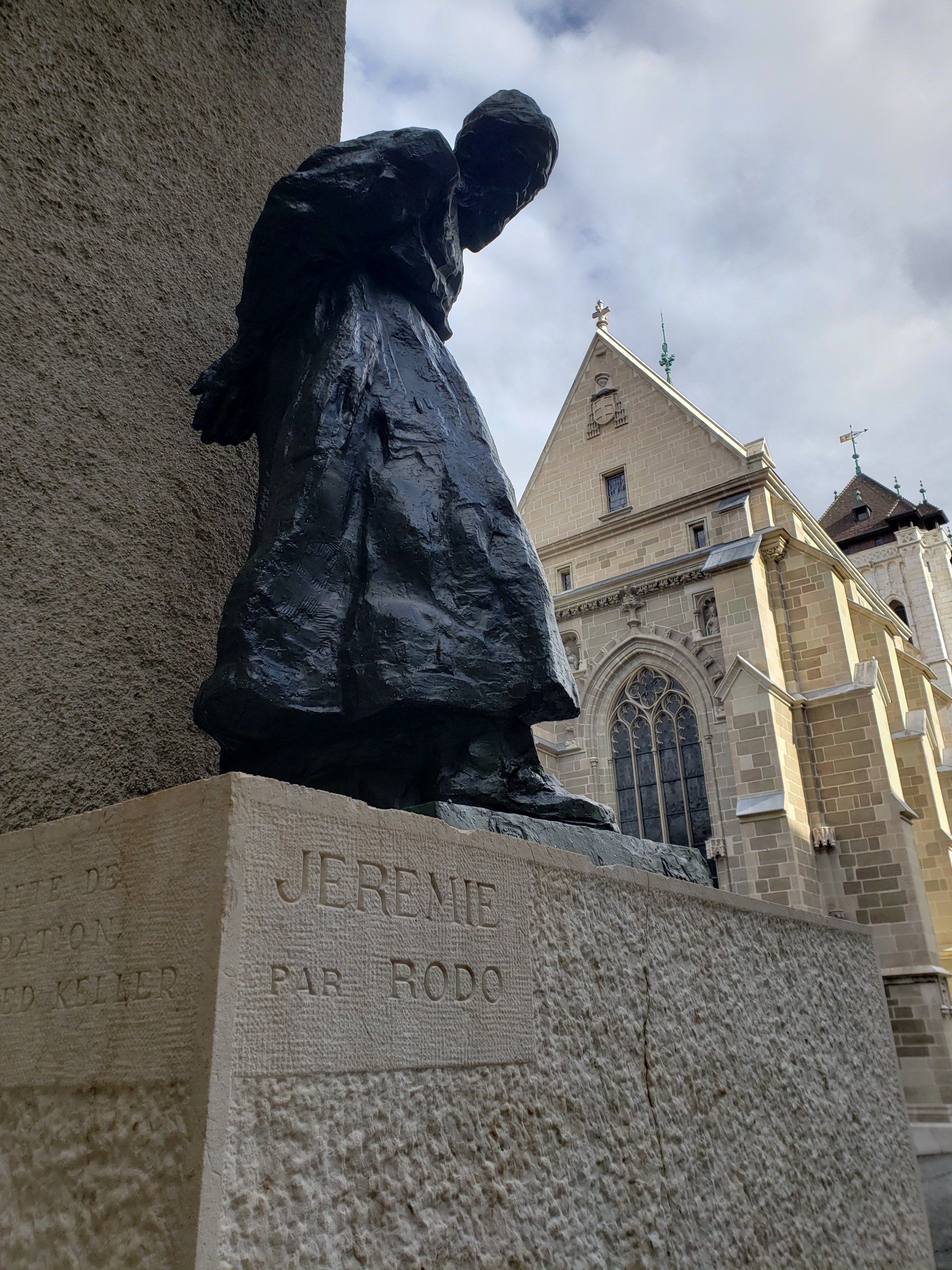 A statue of a man kneeling down in front of a church.