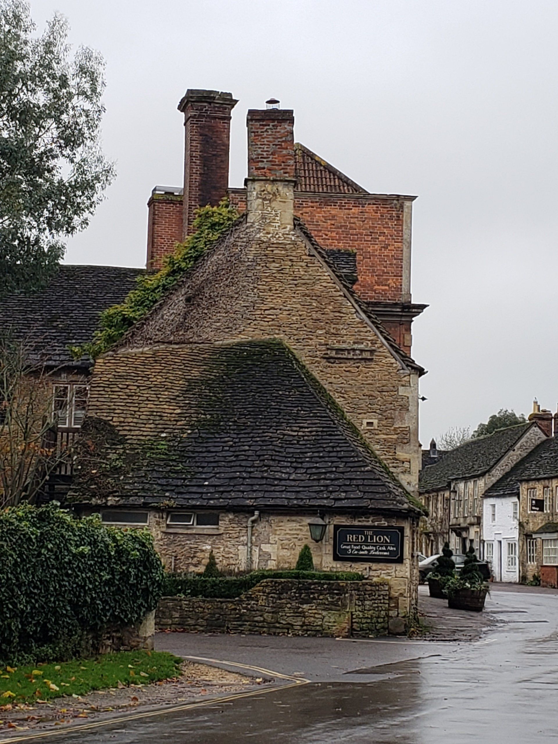 A stone building with a slate roof and chimneys on a rainy day.