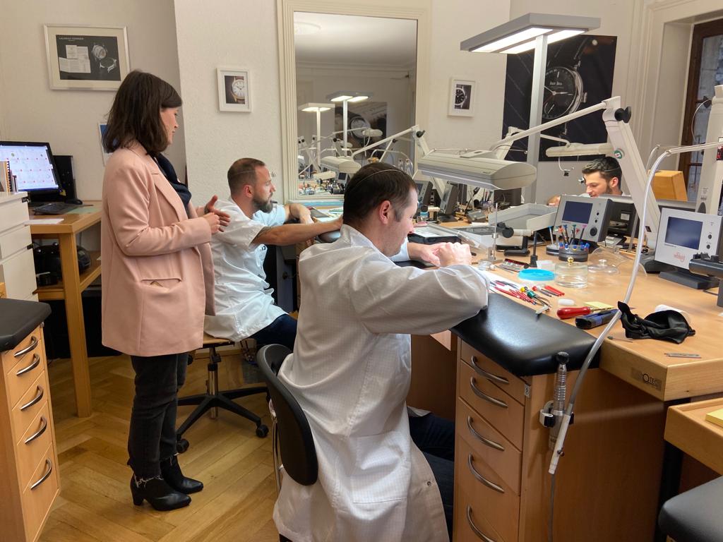 A woman is standing next to a man in a lab coat working on a watch.