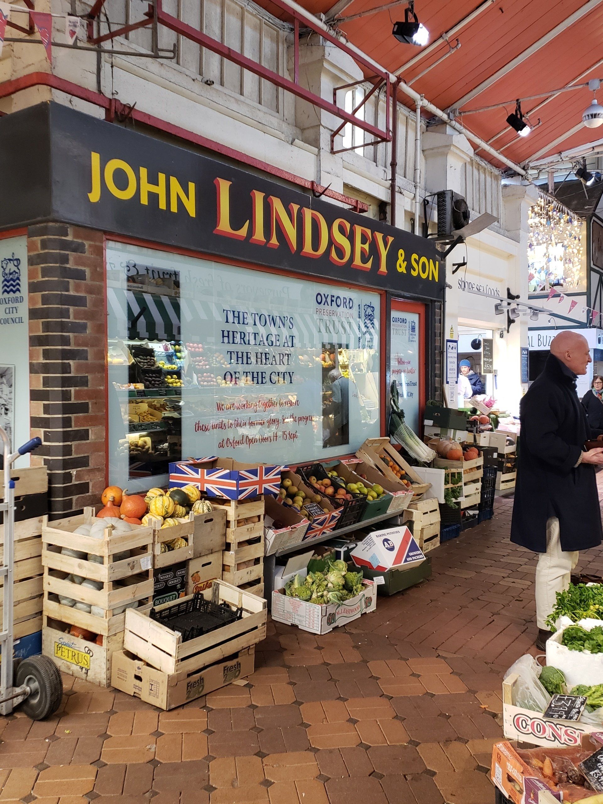 A man is standing in front of a store called john lindsey & son