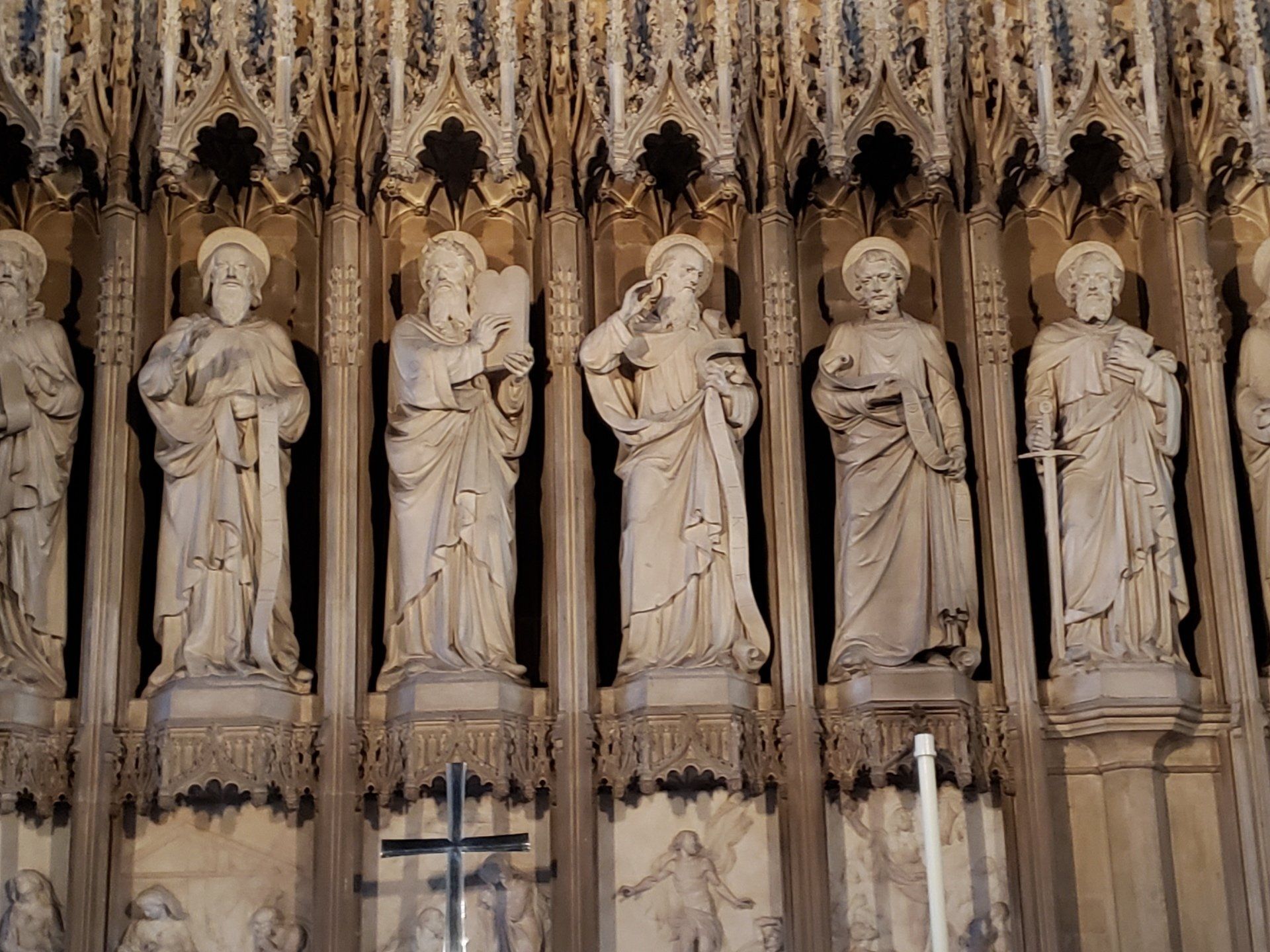 A row of statues of saints in a church with a cross in the background.