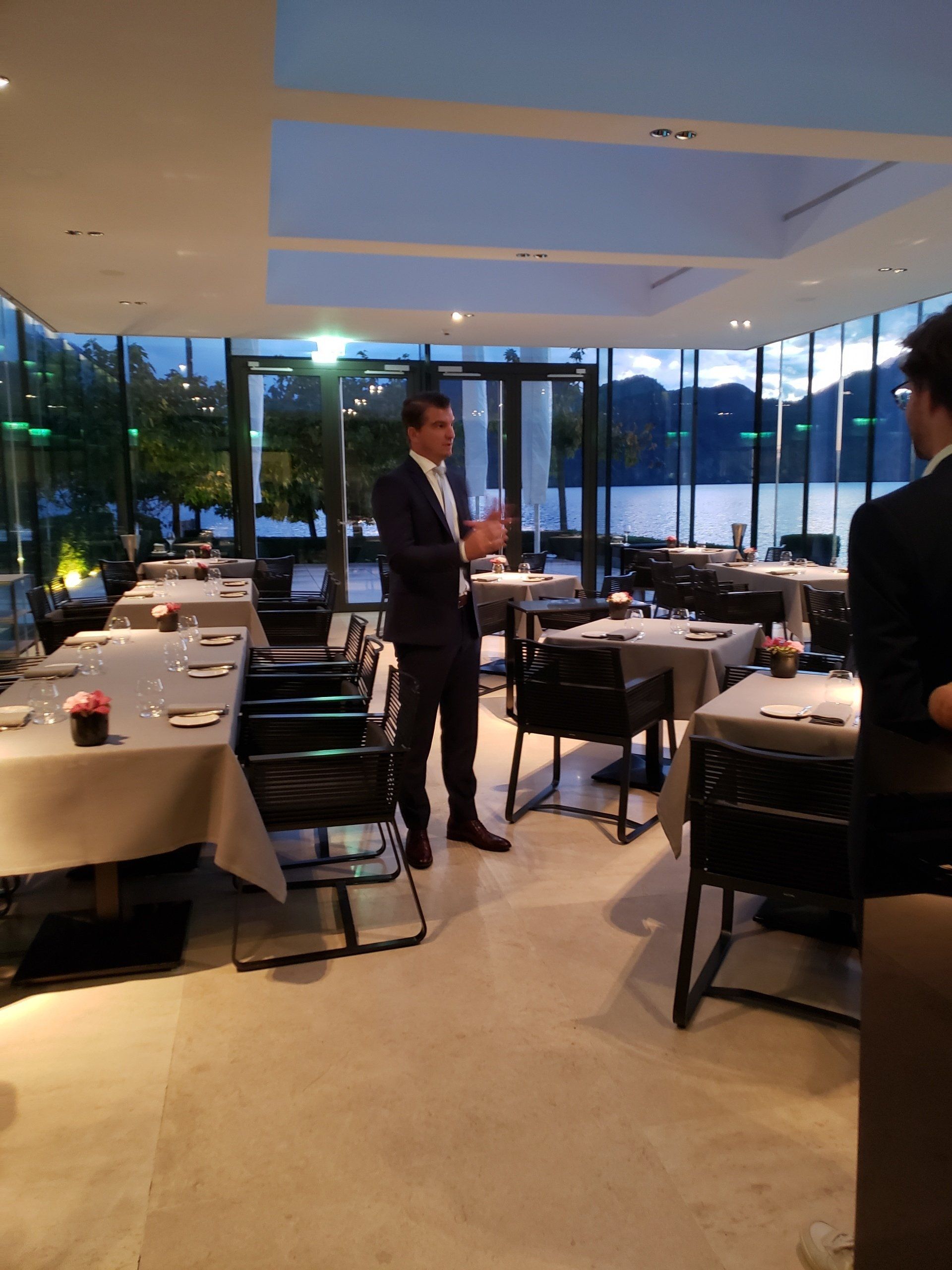 A man in a suit stands in a restaurant with tables and chairs