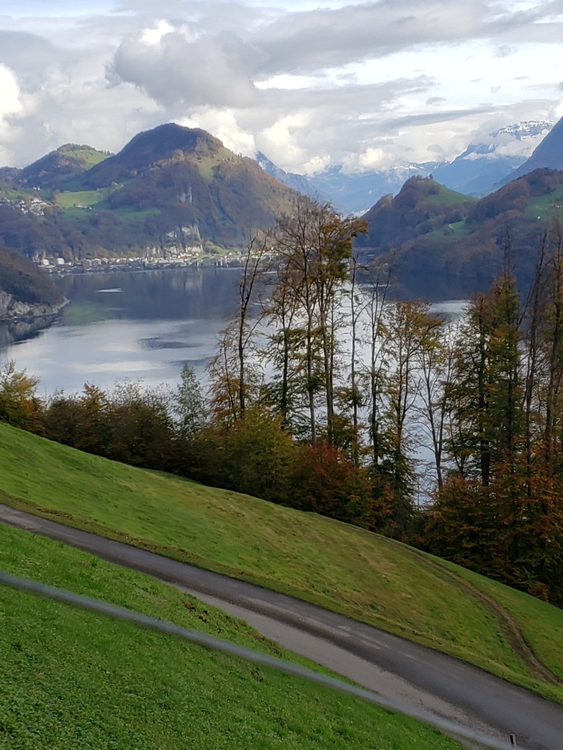 A road going down a hill next to a lake with mountains in the background.