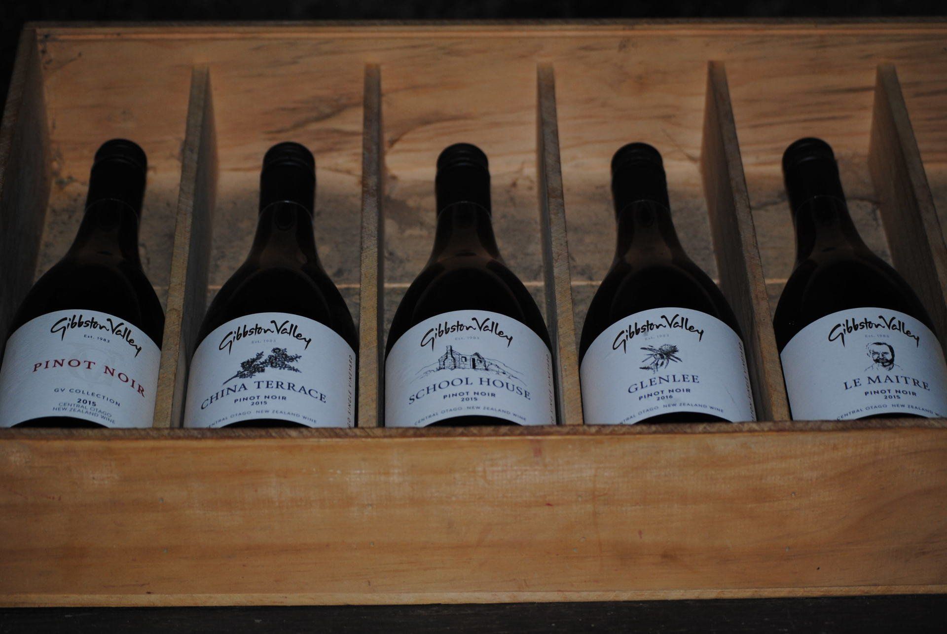Six bottles of wine are lined up in a wooden box
