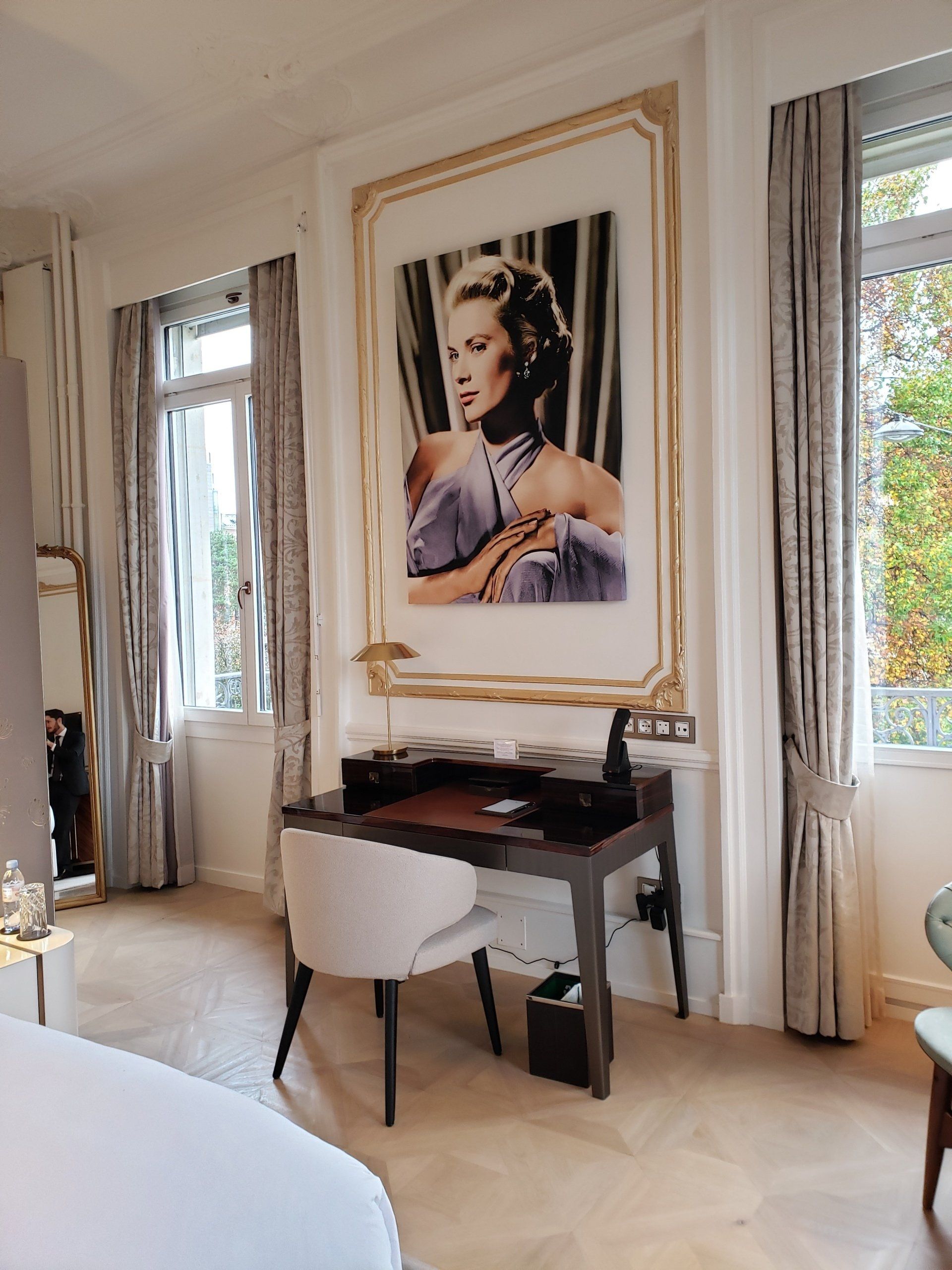 A bedroom with a large painting of a woman on the wall above a desk.