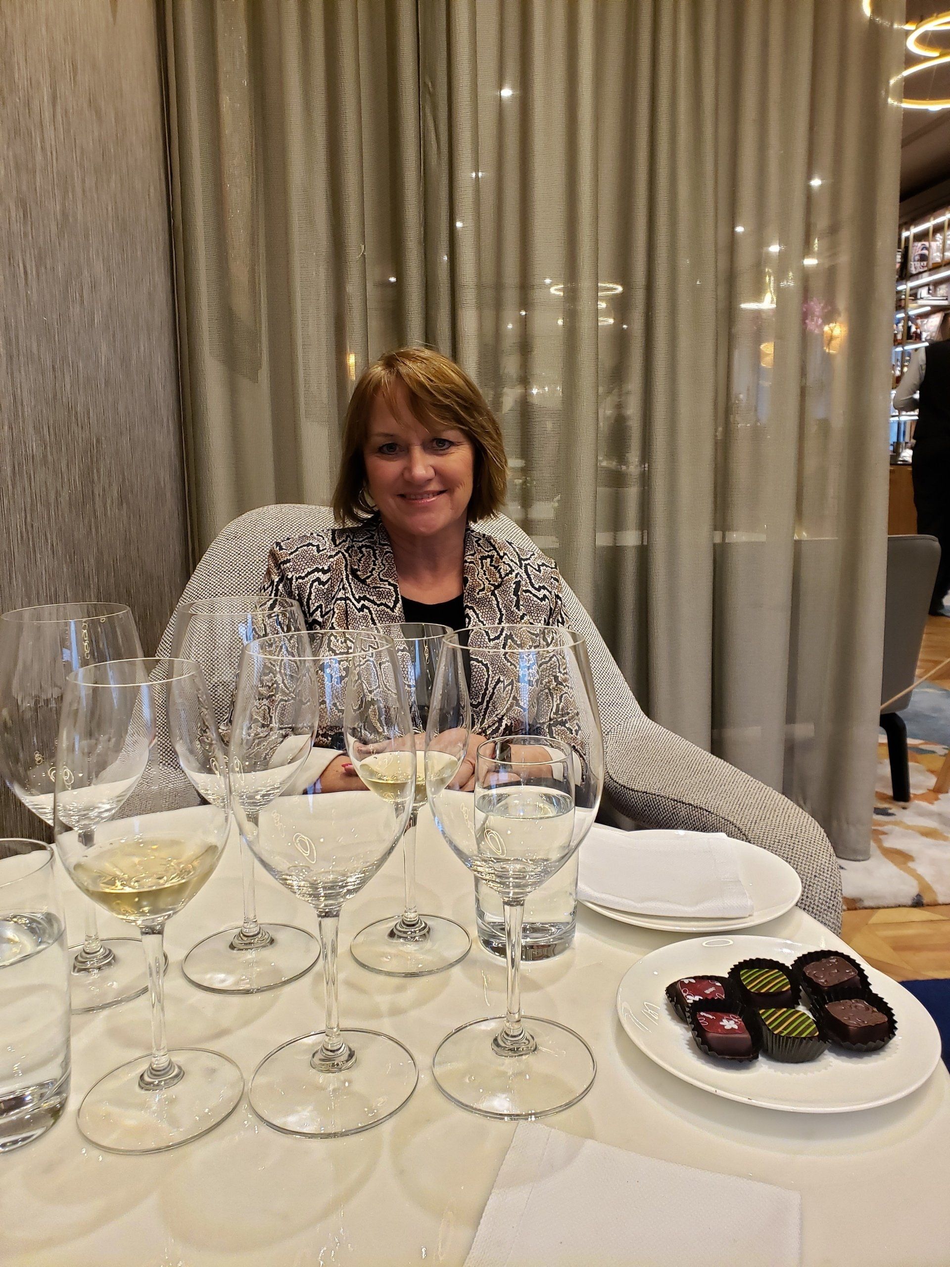 A woman is sitting at a table with wine glasses and chocolates.