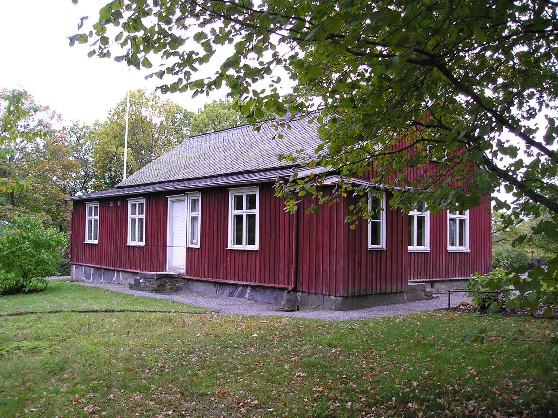 A red house with white windows is surrounded by trees