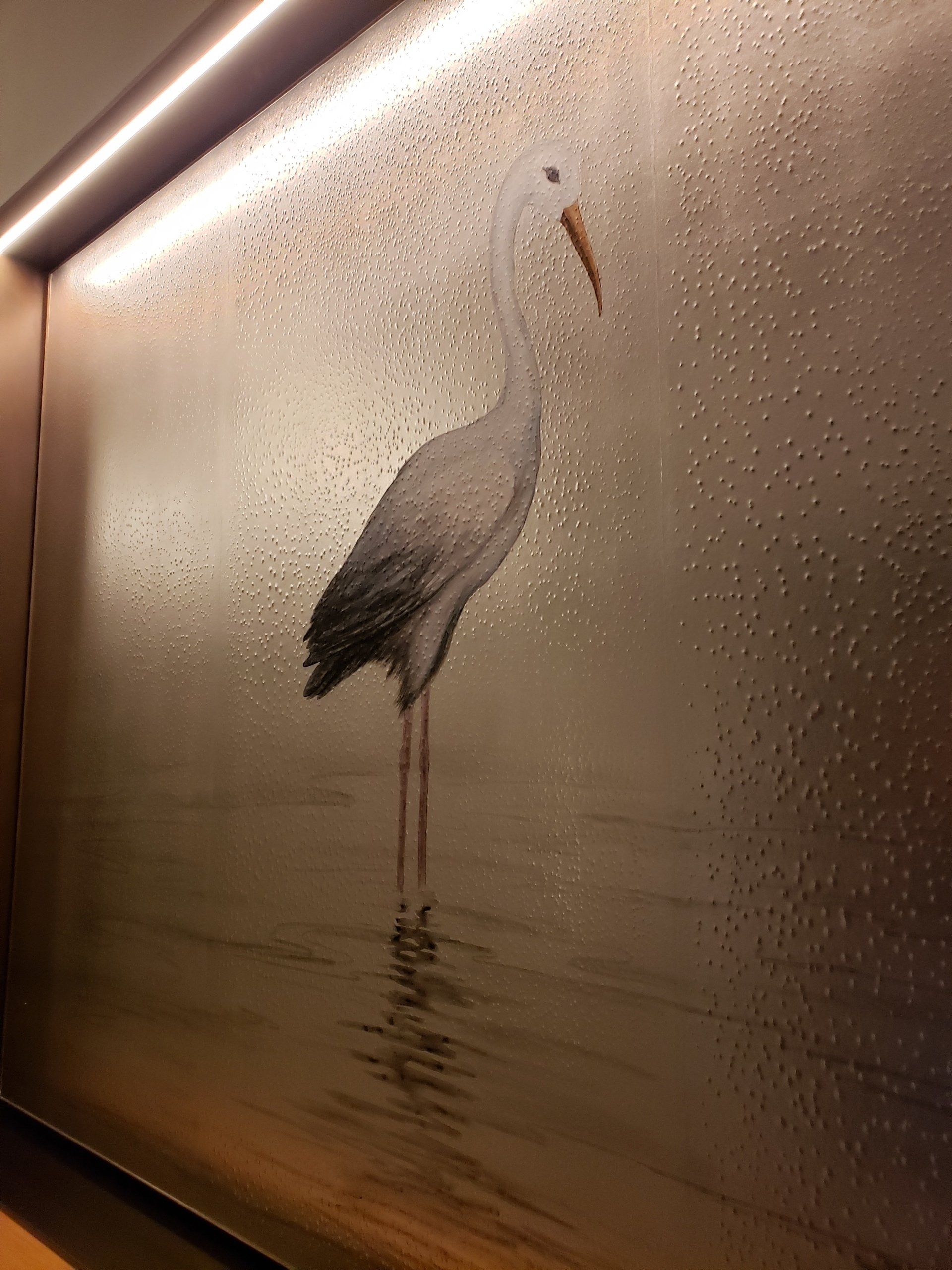 A painting of a bird standing in the water on a wall.