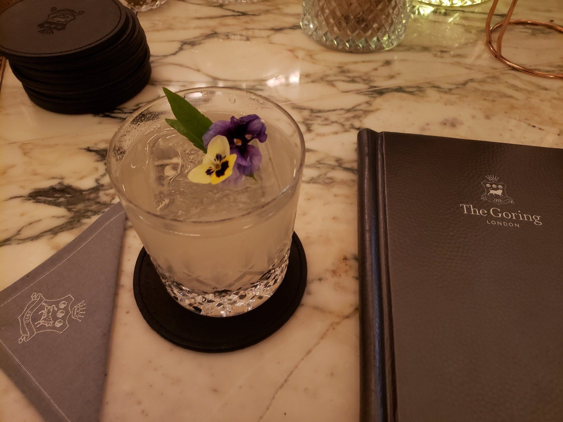A drink with a flower in it sits on a coaster next to a menu