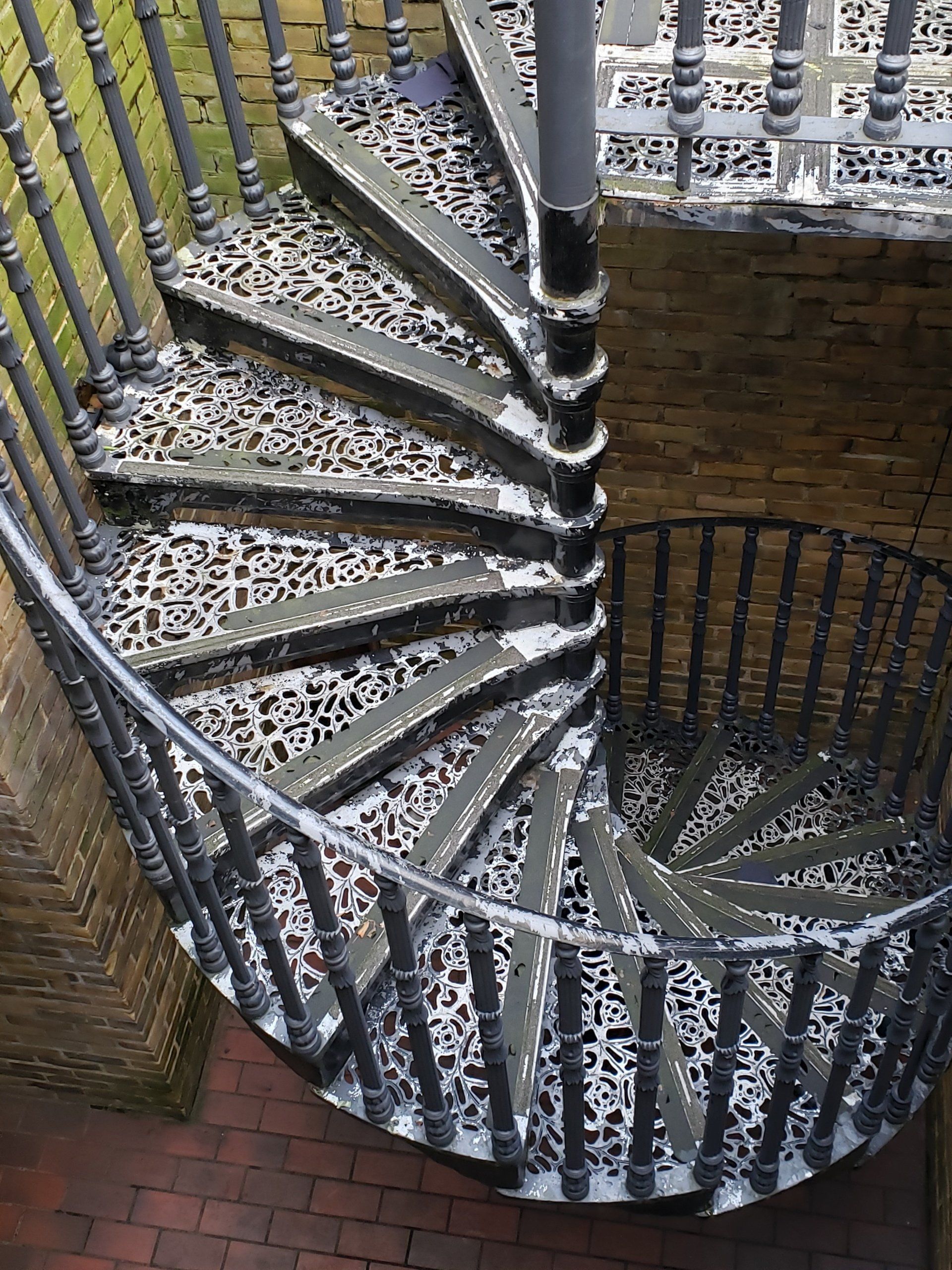 A spiral staircase with a wrought iron railing leading up to a brick wall.