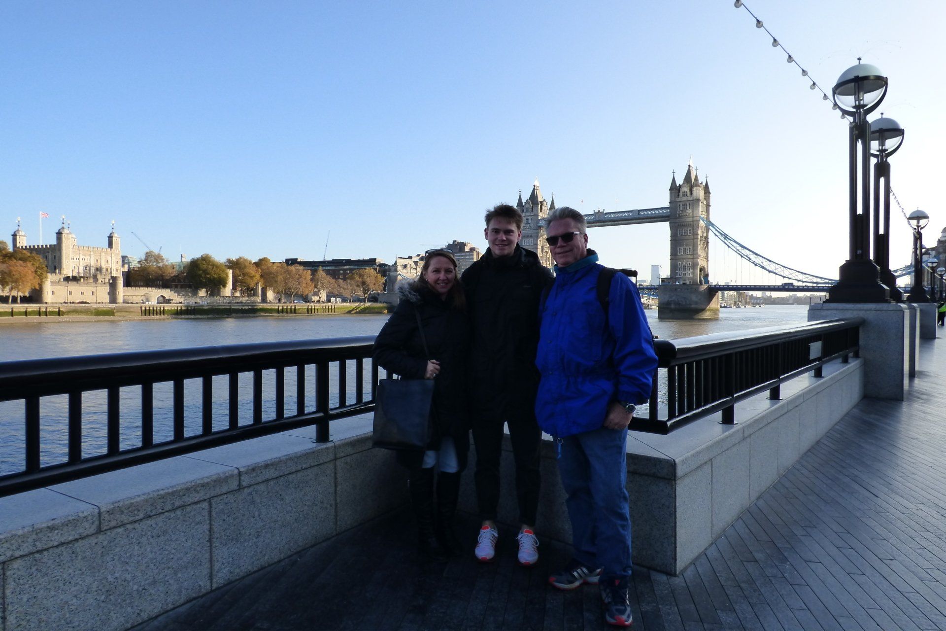 Three people are posing for a picture in front of the tower bridge in london